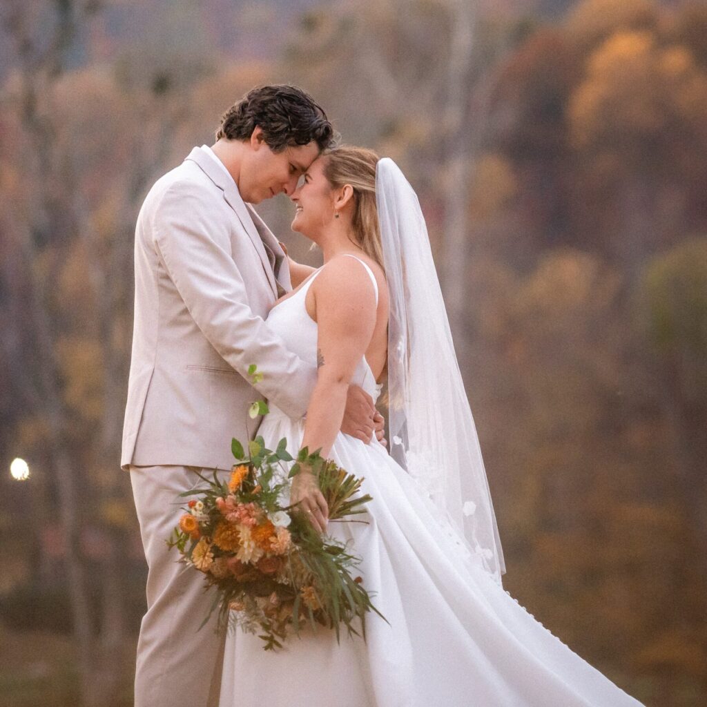 A bride and groom looking into eachother's eyes and embracing in front of autumn leaves on a mountain